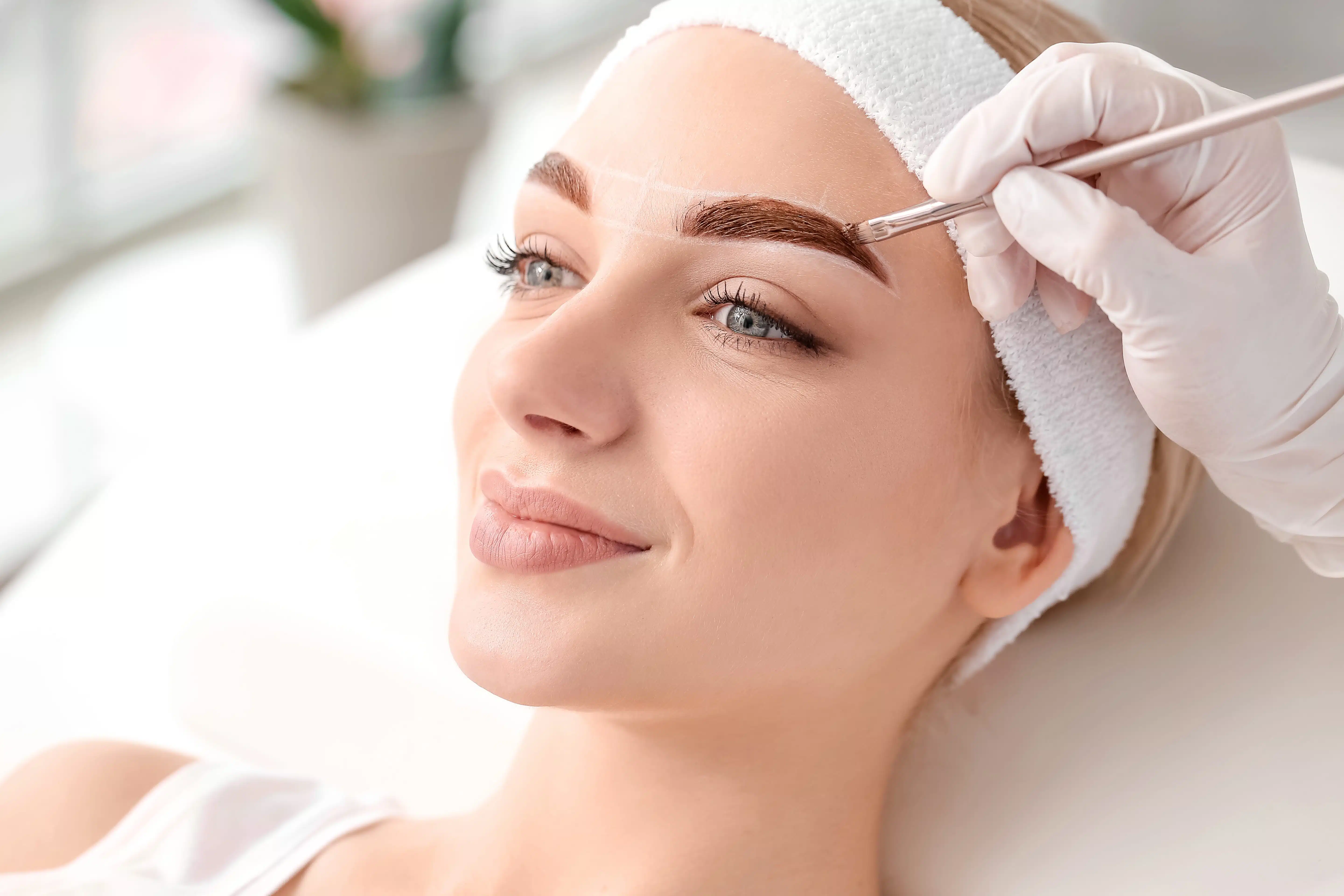 Young woman undergoing eyebrow correction procedure in beauty salon