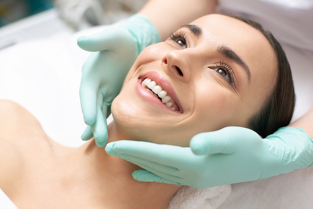 Beautician massaging the face of young lady in rubber gloves