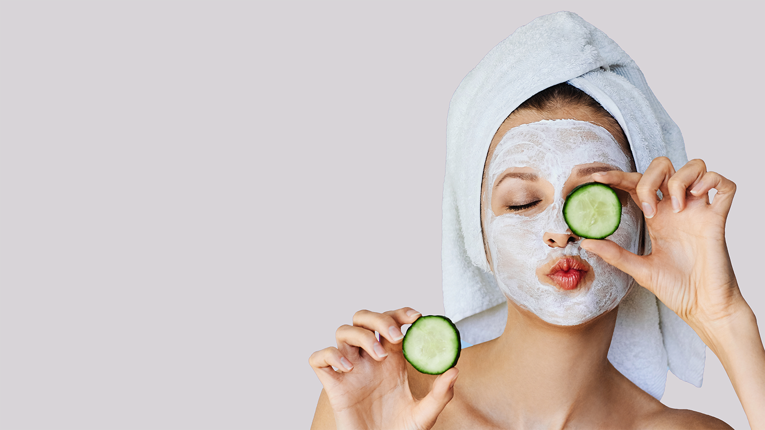 Beautiful Young Woman With Facial Mask On Her Face Holding Slices Of Cucumber