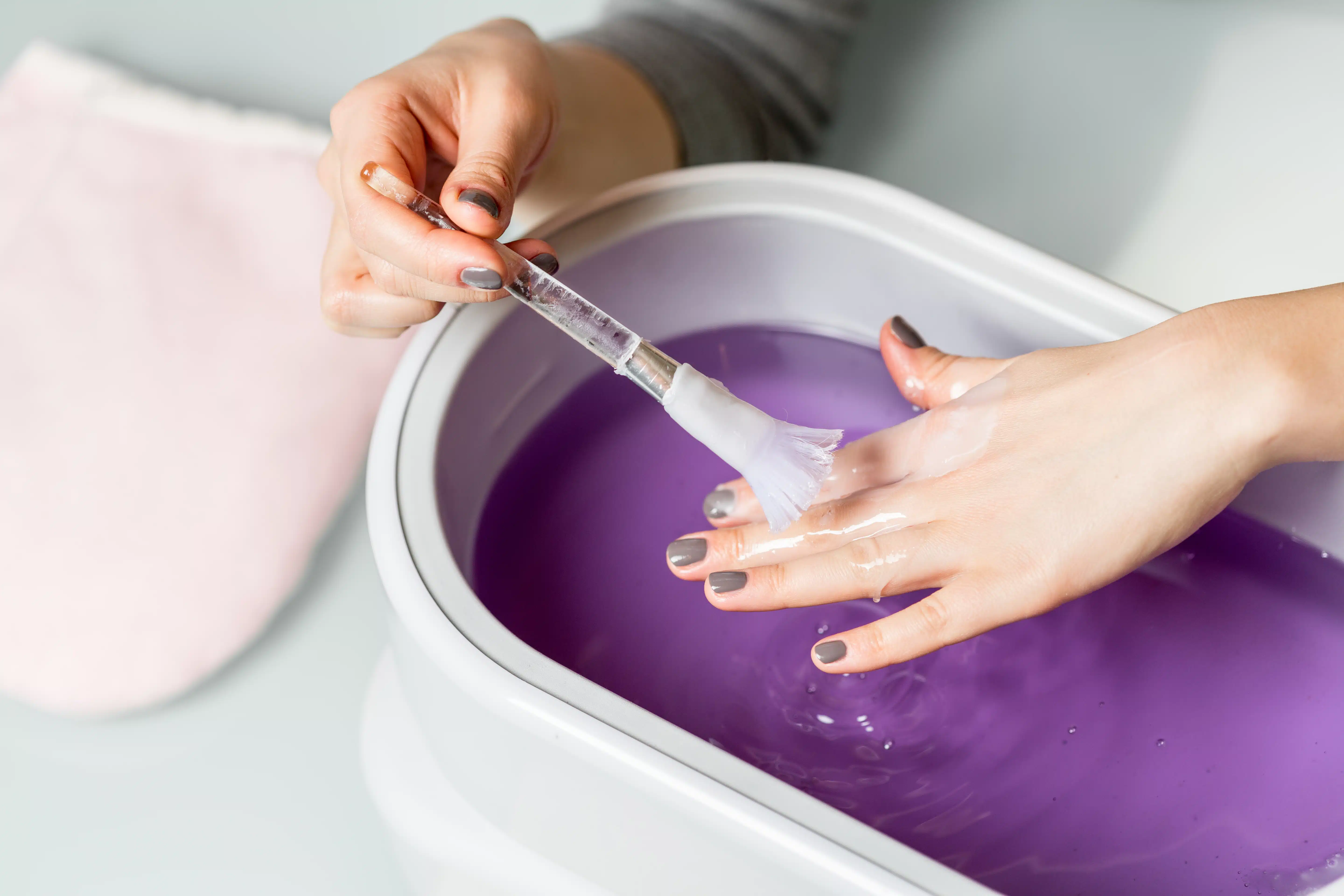 Female hands taking procedure in a lilac paraffin wax bowl