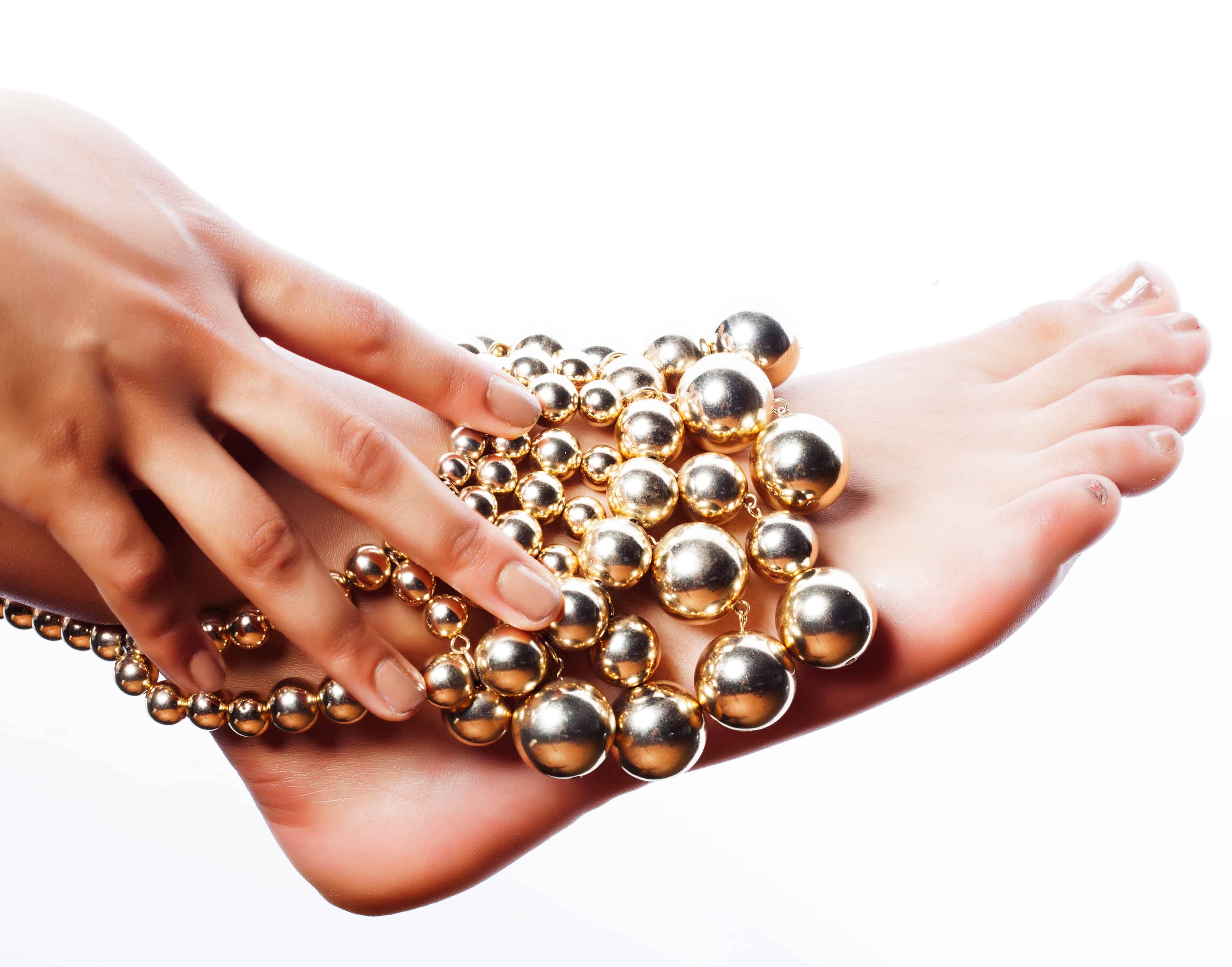 Taned hands with manicure and foot pedicured holding gold balls jewelry isolated on white background, spa salon people concept closeup