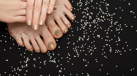 Female hands with golden nail design. Glitter gold nail polish pedicure. Female hands and feet with golden stars on black background with copy space.