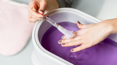 Female hands taking procedure in a lilac paraffin wax  bowl. Cosmetological and skincare equipment in a beauty & spa salon.