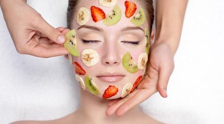 Cosmetician doing fruit mask on a face of beautiful young woman - indoors