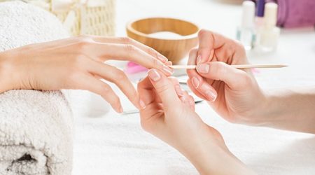 Closeup shot of a woman using a cuticle pusher to give a nail manicure. Nail technician giving customer a manicure at nail salon. Young caucasian woman receiving a french manicure.