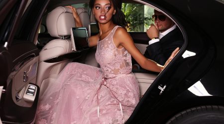 fashion photo of gorgeous mulatto woman with long dark hair wears luxurious dress and man in elegant costume,arrived on red carpet event in black car
