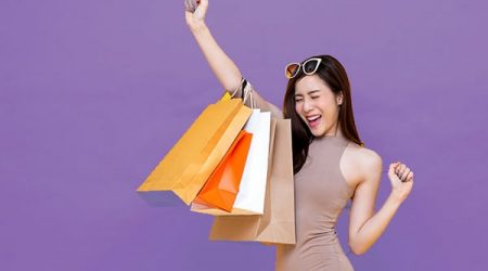 Happy excited Asian woman carrying shopping bags with hand raising up studio shot isolated on colorful yellow background